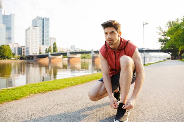 Şehir nehir kenarında çalışırken kulaklık kullanan ve ayakkabı bağcıklarını bağlayan adam fotoğrafı