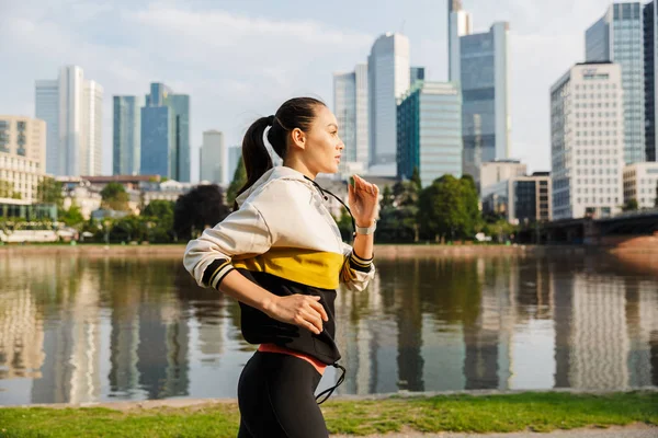 Foto de una mujer delgada y deportiva corriendo mientras hace ejercicio cerca de la ribera de la ciudad — Foto de Stock