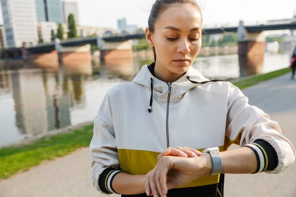 Photo d'une femme sportive concentrée utilisant un chronomètre tout en s'entraînant près du bord de la rivière de la ville — Photo