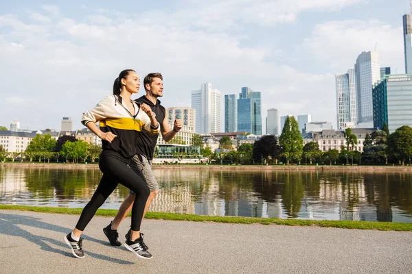 Foto de morena seria hombre y mujer haciendo ejercicio y corriendo en la ciudad frente al río — Foto de Stock