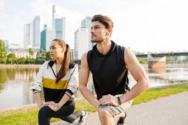 Foto de un hombre y una mujer jóvenes enfocados haciendo ejercicios mientras hacen ejercicio en la ribera de la ciudad — Foto de Stock