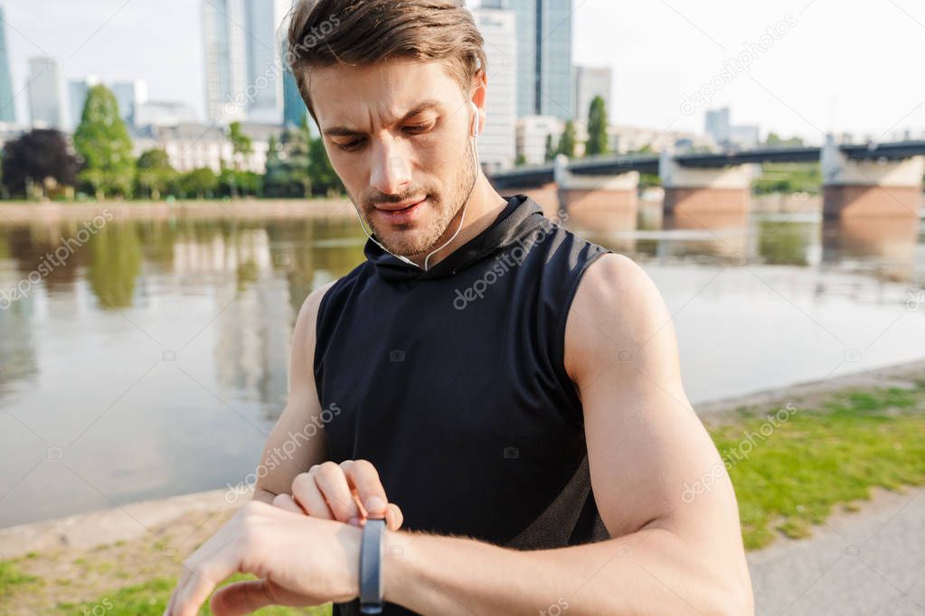 Photo of brooding caucasian man using stopwatch while working out on city riverfront