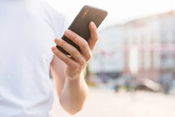 Close-up van een man in wit t-shirt houden mobiele telefoon — Stockfoto