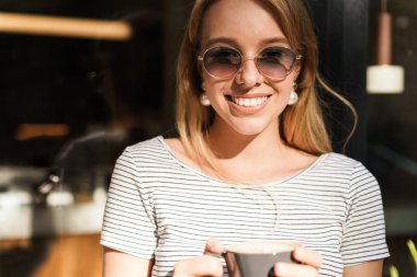 Kafe açık havada sokakta dururken gülümseyen ve kahve fincanı tutan şık kadın portresi