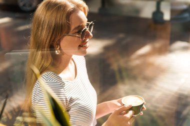 Sokak kafeaçık otururken gülümseyen ve kahve fincanı tutan büyüleyici genç kadın görüntü