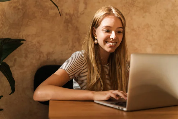 Retrato de una mujer joven y bonita usando un ordenador portátil mientras está sentado en la cafetería —  Fotos de Stock