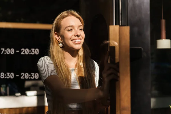 Porträt einer fröhlichen jungen Frau, die beim Verlassen eines Cafés oder Kaffeehauses eine Glastür öffnet — Stockfoto