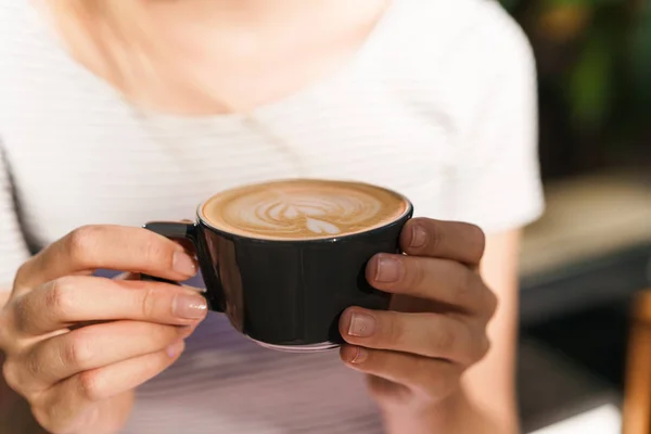 Обрізане зображення кавказької молодої жінки, що тримає чашку кави латте в кафе — стокове фото