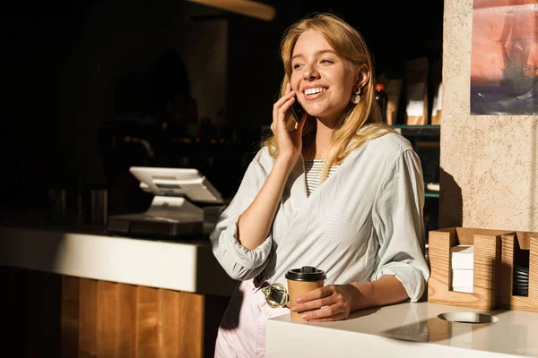 Портрет молодої оптимістичної жінки, що розмовляє по смартфону під час випивки кави в кафе — стокове фото