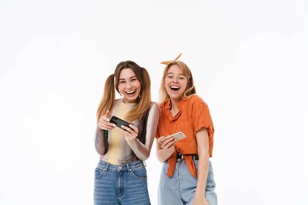 Foto de duas meninas bonitas vestindo roupas coloridas rindo enquanto segurando smartphones juntos — Fotografia de Stock