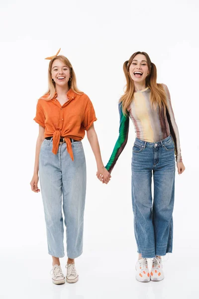 Foto de comprimento total de duas meninas bonitas vestindo roupas coloridas sorrindo para a câmera enquanto segurando as mãos juntas — Fotografia de Stock