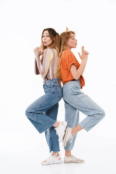 Foto di due ragazze fighe che indossano vestiti colorati in piedi dietro e fanno il gesto della pistola con le dita — Foto Stock