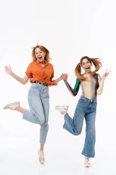Foto a figura intera di due ragazze gioiose che indossano vestiti colorati ridendo e divertendosi mentre si tengono per mano insieme — Foto Stock