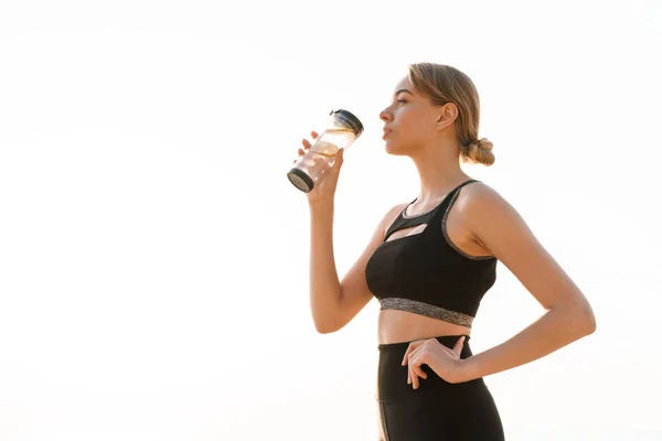 Bild der niedlichen konzentrierten Frau, die morgens Wasser aus Plastikbechern in der Nähe des Meeres trinkt — Stockfoto