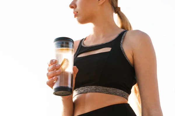 Cropped image of cute concentrated woman drinking water from plastic cup near seaside in morning — Stock Photo, Image