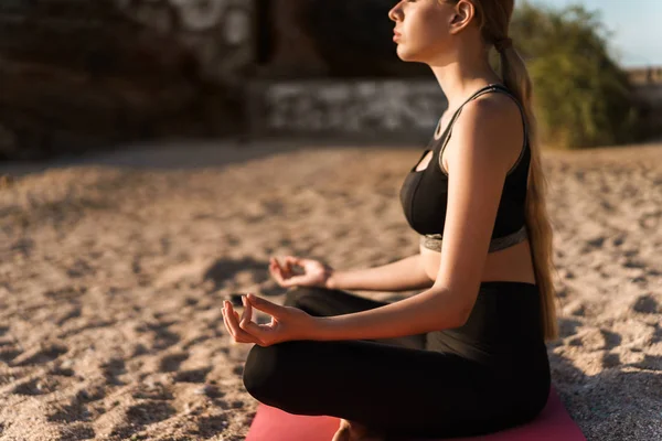 Bild av blond fokuserad kvinna som editerar med fingrarna tillsammans medan du sitter på yogamattan vid havet på morgonen — Stockfoto