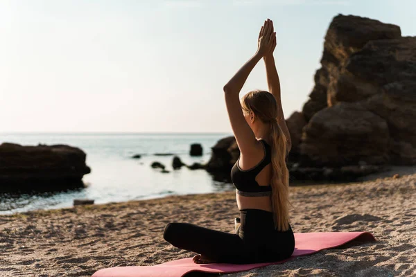 Imagen de una mujer rubia enfocada haciendo ejercicios de yoga en la estera junto al mar por la mañana —  Fotos de Stock