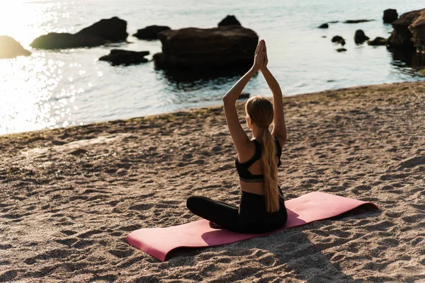 Image of sporty focused woman doing yoga exercises on mat at seaside in morning — Stock Photo, Image