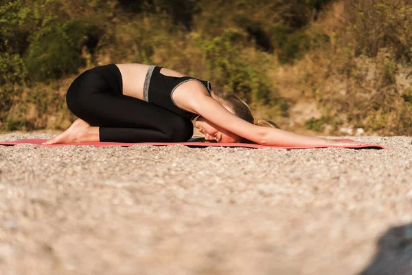 Imagen de la mujer satisfecha concentrada relajándose después de ejercicios de yoga en la estera en la playa por la mañana —  Fotos de Stock