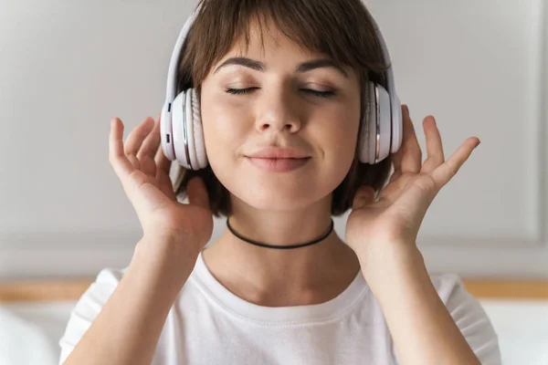 Relajante joven hermosa mujer en el interior de casa escuchando música con auriculares . —  Fotos de Stock