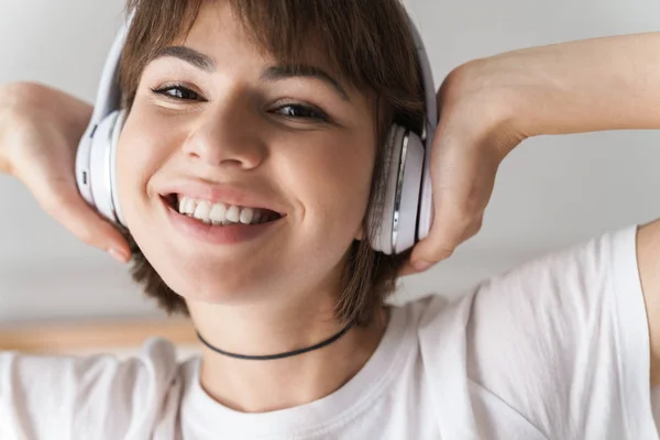 Sonriente joven hermosa mujer en el interior de casa escuchando música con auriculares . —  Fotos de Stock