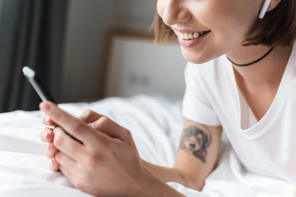긍정적 인 젊은 아름다운 여성은 휴대 전화를 사용하여 블루투스 이어폰으로 음악을 듣는 침대에서 집에 있습니다.. — 스톡 사진