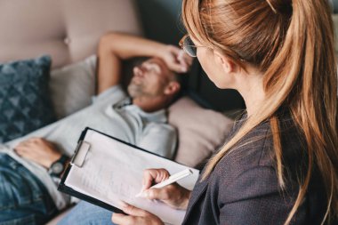 Üzgün beyaz adamın kanepede yatarken ve odada psikologla sohbet fotoğrafı