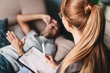 Traşsız rahatsız adam kanepede yatan ve odada psikolog ile konuşma fotoğrafı