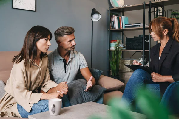 Photo of serious brooding couple having conversation with psychologist on therapy session in room — Stockfoto