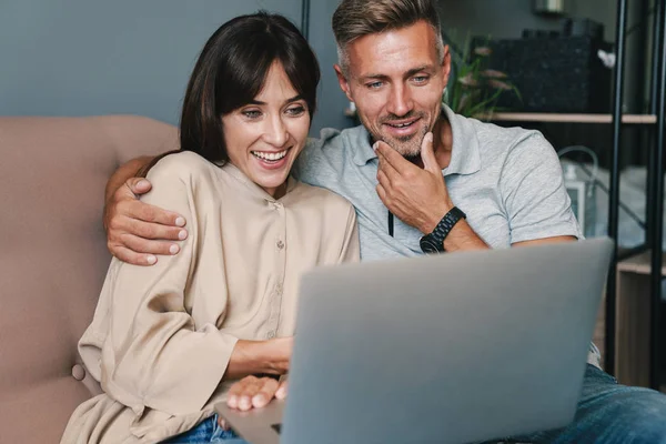 Foto di felice coppia caucasica sorridente mentre guarda il computer portatile sul divano di casa — Foto Stock