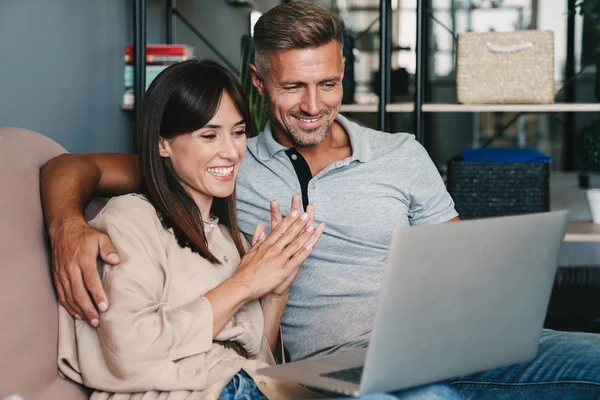 Fotografie veselého kavkazského páru s úsměvem při pozorování laptopu na pohovce doma — Stock fotografie