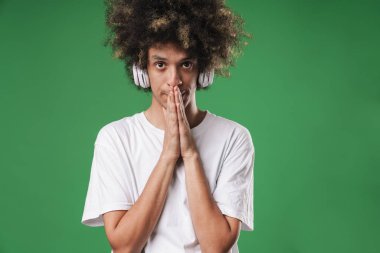 Adam yeşil duvar arka plan üzerinde izole poz kulaklık ile müzik dinleme umutlu jest lütfen olun.