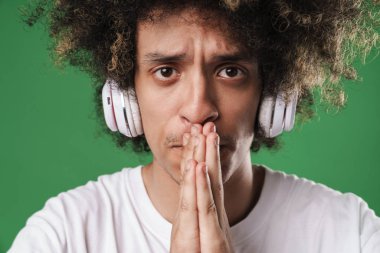 Adam yeşil duvar arka plan üzerinde izole poz kulaklık ile müzik dinleme umutlu jest lütfen olun.