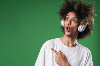Şokkk adam yeşil duvar arka plan üzerinde izole poz kulaklıklar ile müzik dinleme copyspace işaret.