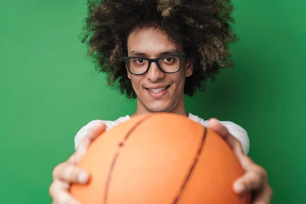 Penutup potret pria tampan tersenyum dengan gaya rambut afro memberikan bola dan melihat kamera terisolasi di atas latar belakang hijau — Stok Foto