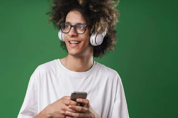 Photo closeup of positive man with afro hairstyle looking aside while using cellphone and headphones — Stock Photo, Image