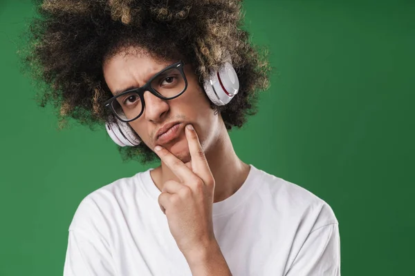 Foto närbild av missnöjd ung man med afro frisyr röra hakan och använda hörlurar — Stockfoto