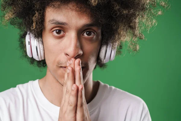 Guy poseren geïsoleerd over groene muur achtergrond luisteren muziek met hoofdtelefoon maken hoopvolle please gebaar. — Stockfoto
