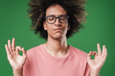 Konsantre kıvırcık adam yeşil duvar arka plan üzerinde izole poz meditasyon.