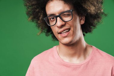 Genç kıvırcık adam yeşil duvar arka plan üzerinde izole poz size göz kırpma.