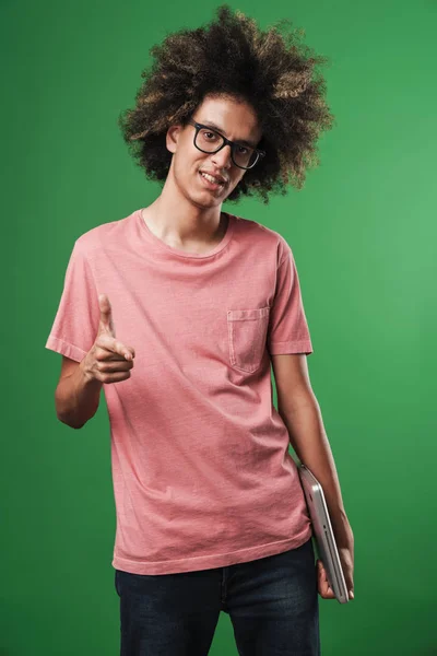 Positivo chico rizado complacido posando aislado sobre fondo de pared verde sosteniendo ordenador portátil que apunta a usted . — Foto de Stock