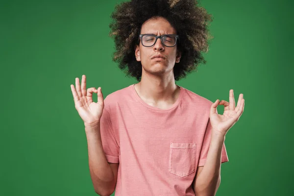 Concentrated curly guy posing isolated over green wall background meditate. — Stock Photo, Image