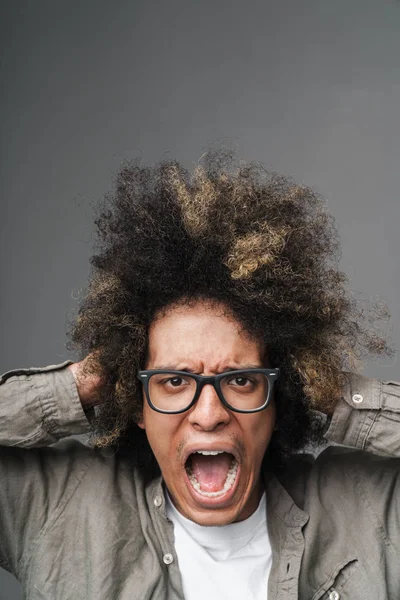 Foto close-up van beklemtoonde jonge man met Afro kapsel grijpen zijn hoofd en schreeuwen en geïsoleerd over grijze achtergrond — Stockfoto