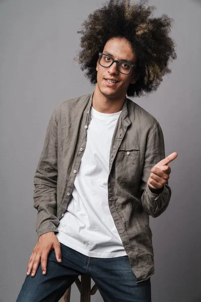 Foto van tevreden ongeschoren man met Afro kapsel zittend op stoel en wijzende vinger vooruit — Stockfoto