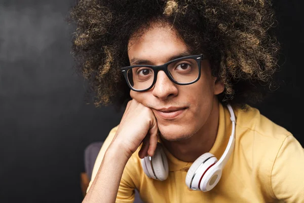 Curly young pleased teenage guy posing over grey chalkboard wall with headphones. — Stock Photo, Image