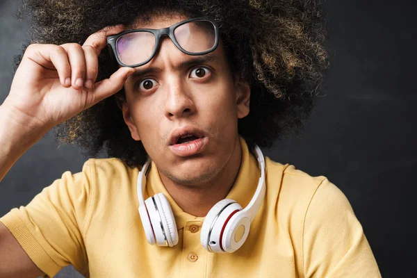 Bang tiener kerel poseren over grijs schoolbord muur met hoofdtelefoon dragen brillen. — Stockfoto