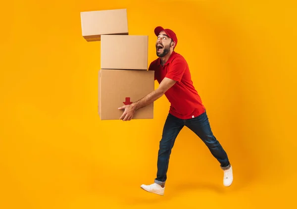 Full length portrait of funny delivery man in red uniform carryi — Stock Photo, Image