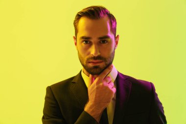 Kendine güvenen genç işadamının çenesini dokunup kameraya baktığı resmi takım elbiseli görüntüsü