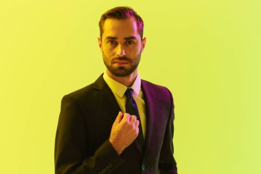 Ceketine dokunan ve kameraya bakan resmi takım elbiseli kendinden emin genç işadamının görüntüsü