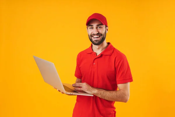 Portret szczęśliwego człowieka dostawy w czerwonym t-shirt i czapka uśmiechnięta i trzymając srebrny komputer przenośny — Zdjęcie stockowe